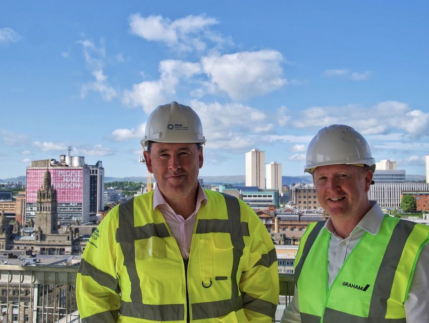 Graeme Bone, Group Managing Director, Drum Property Group (left), Dan Batterton, Head of Residential at Legal & General Investment Management Real Assets (right) in hi-vis and hard hats. They stand on top of a building with the Glasgow skyline in the background.