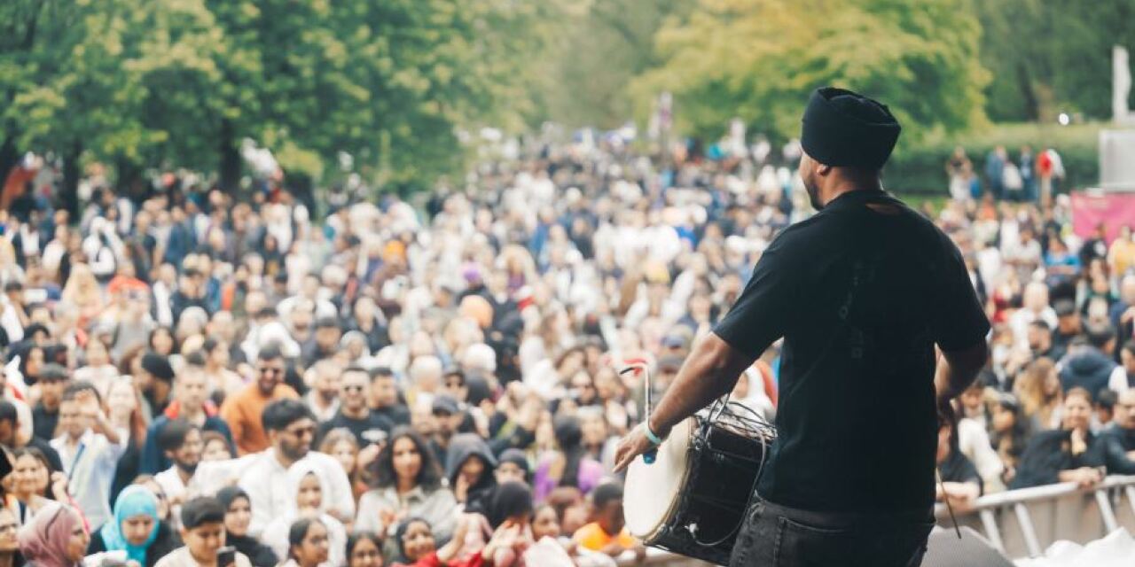 A man playing a drum and facing a large audience