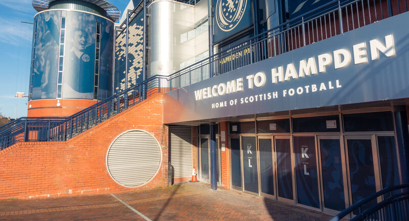 A colour photo of the main entrance to Hampden Park. White lettering on a blue background proudly announces: WELCOME TO HAMPDEN. HOME OF SCOTTISH FOOTBALL. Image Courtesy of Getty.