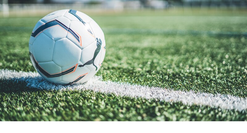 A white football with black stitching sits on a crisp white line, the grass is green.