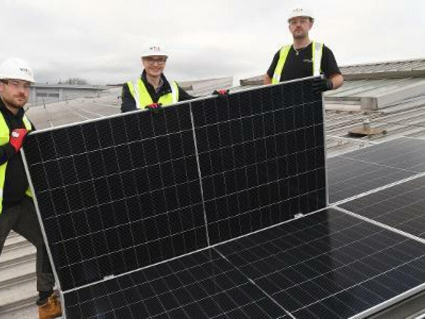 3 men in hi vis workwear are installing solar panels on a roof
