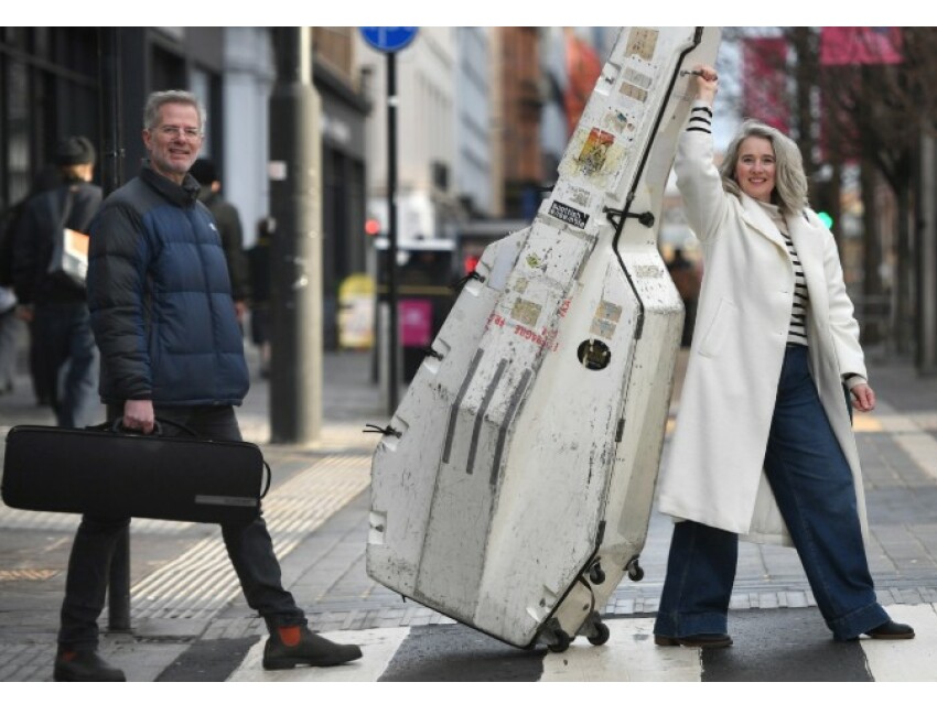 Three people carrying musical instruments walking over a crosswalk in Sauchiehall Street.